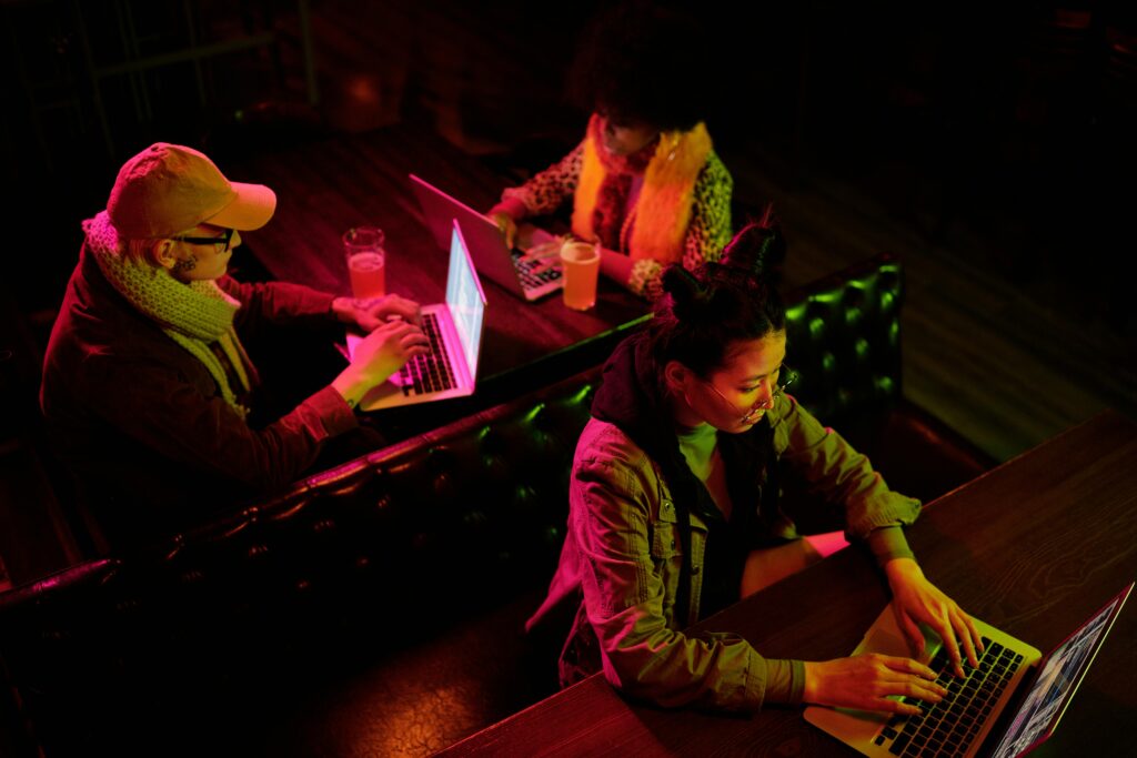 A diverse group of individuals working on laptops in a low-lit indoor environment, highlighting teamwork and technology.
